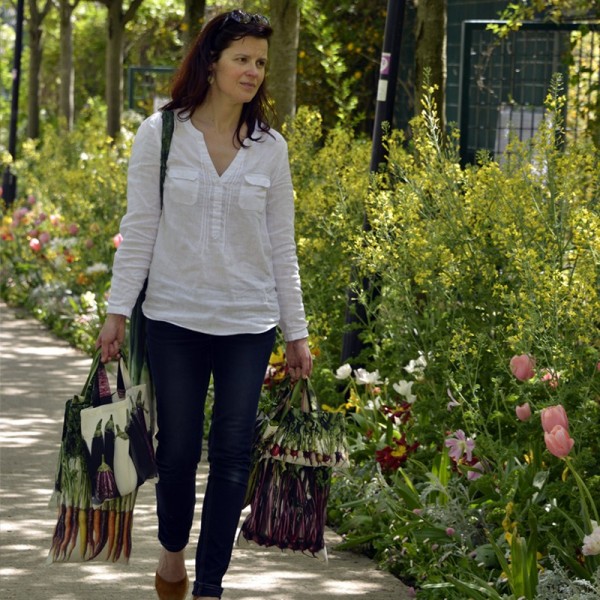 Femme traversant un jardin avec les sacs de courses de Maron Bouillie dans les mains. Sacs légumes made in France