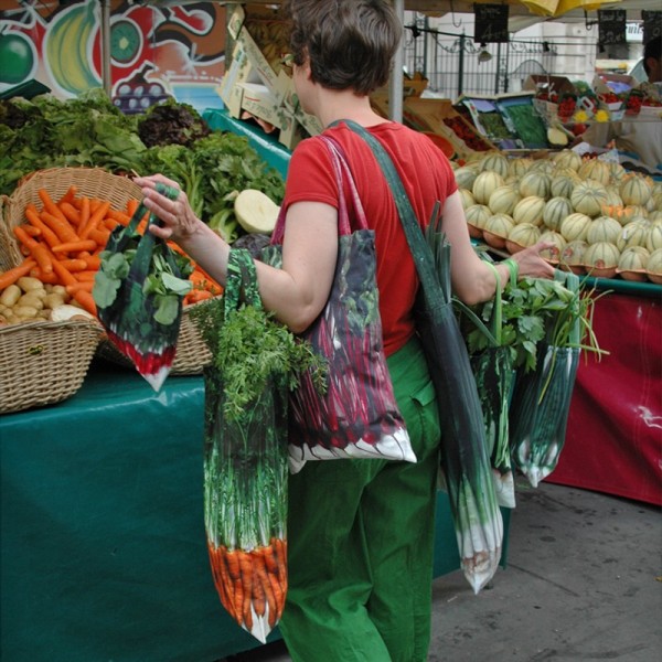 Maron Bouillie portant les sacs de courses légumes devant un étal de marché à Paris.