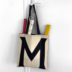 Sac lettre M de Maron Bouillie accroché à la poignée d'une porte - Idée Cadeau d’anniversaire femme original.