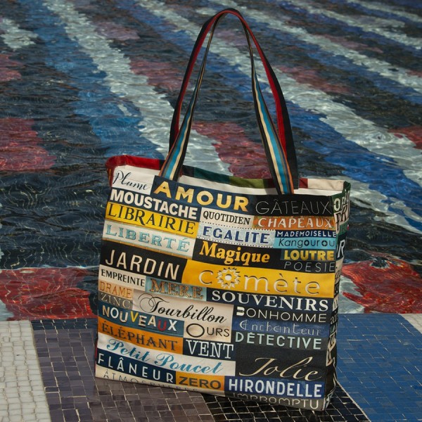 Alphabet shopping bag with colored words placed on the edge of a pond - Maron Bouillie Paris