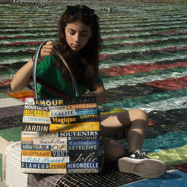 Young girl sitting at the edge of a pool with the shopping bag alphabet words by Maron Bouillie made in France