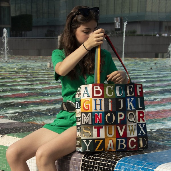 Young girl sitting at the edge of a pool with the shopping bag alphabet letters by Maron Bouillie made in France