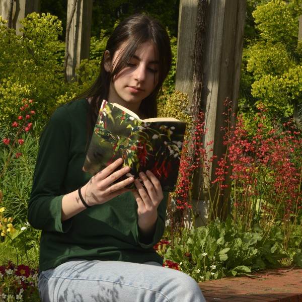 Une jeune fille dans un jardin, lit un livre avec la couverture de livre fleur fuchsia de Maron Bouillie. Une jeune fille dans un jardin, lit un livre avec la couverture de livre fleur fuchsia de Maron Bouillie.
