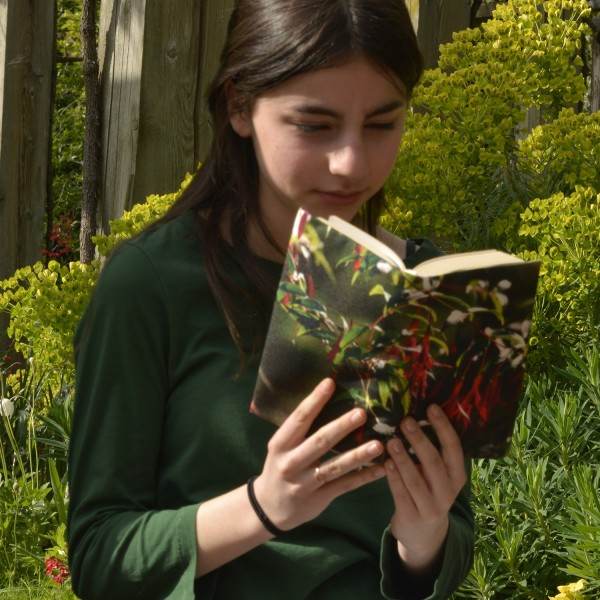 Une jeune fille dans un jardin, lit un livre avec la couverture de livre fleur fuchsia de Maron Bouillie. Plan rapproché Une jeune fille dans un jardin, lit un livre avec la couverture de livre fleur fuchsia de Maron Bouillie. Plan rapproché