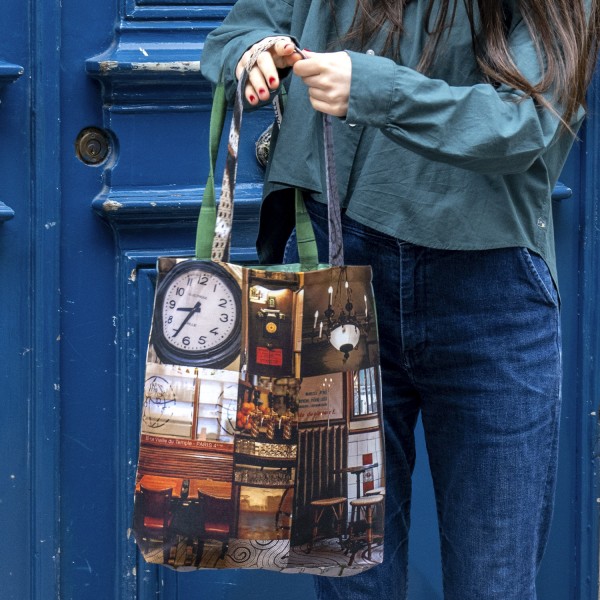 Tote bag Paris Café Au petit fer à cheval in the hands of a woman in front of a blue door. Maron Bouillie