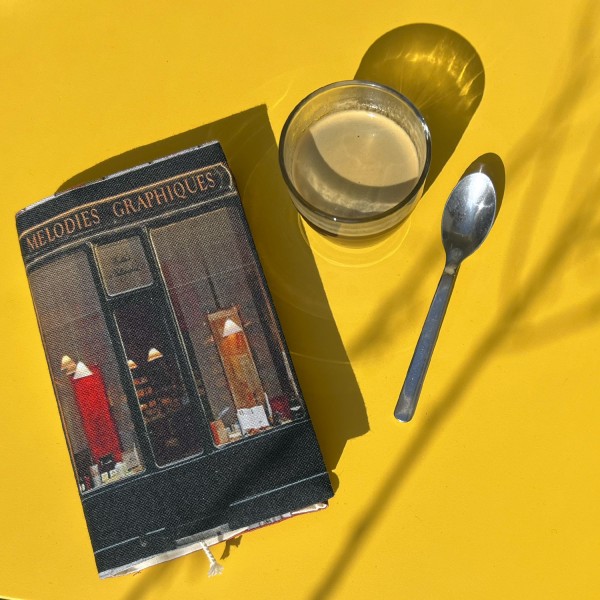 Protège-livre Paris Boutique Mélodies graphiques Calligraphies posé sur une table jaune avec un café - Maron Bouillie