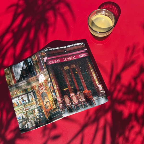 Couvre-livre de poche Café de Paris Le royal posé sur une table rouge avec des ombres végétales - Maron Bouillie made in France